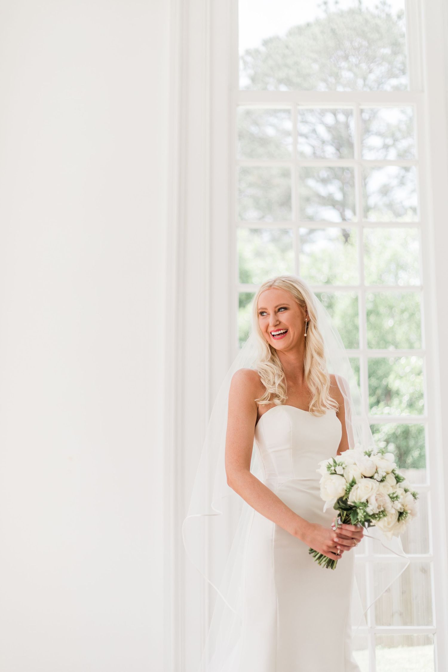 Bright and airy wedding photo in white room with large windows and natural light.