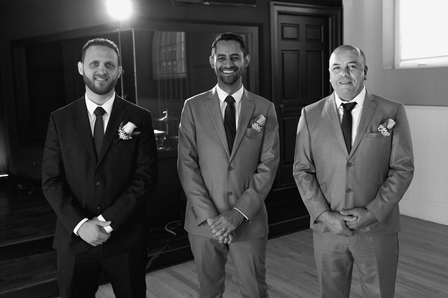 Three groomsmen in formal attire stand together during a wedding.