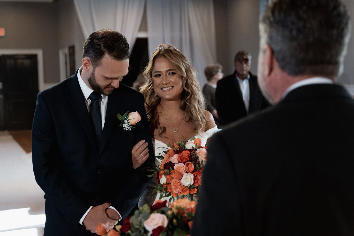 Wedding ceremony with guests in background and floral decorations.
