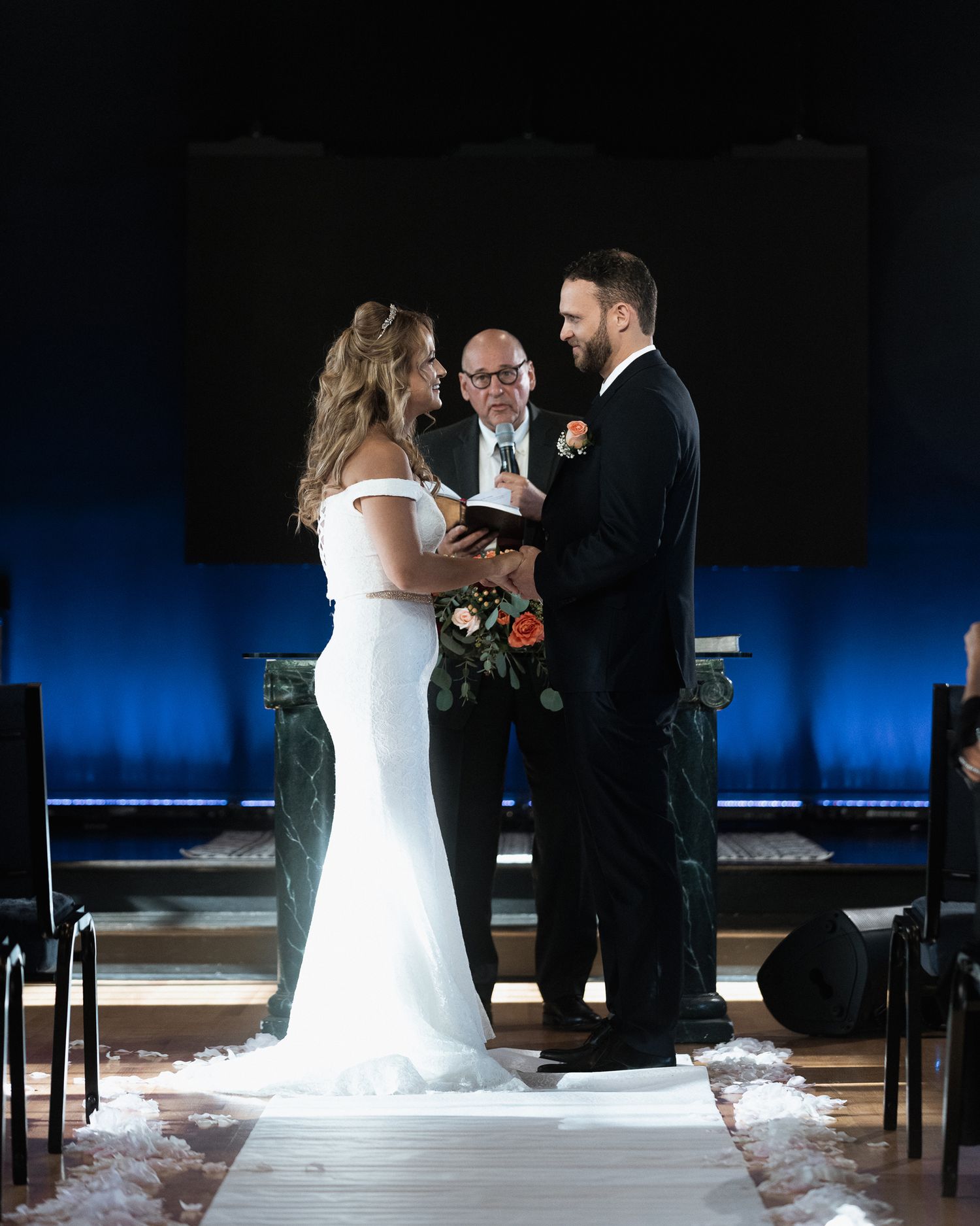 A wedding ceremony takes place on a stage with dramatic blue lighting.