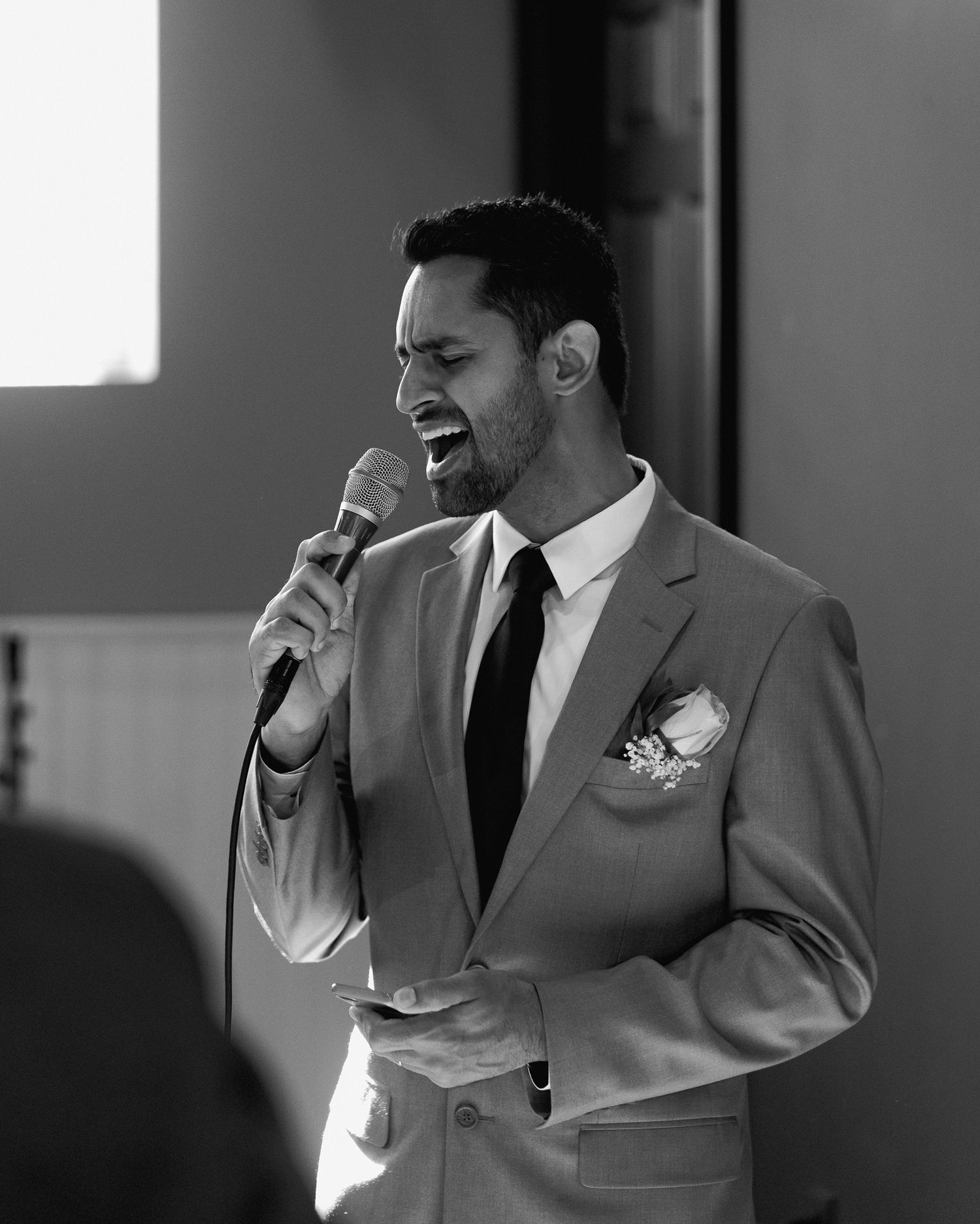 A suited guest delivers a speech with a microphone during a wedding reception.