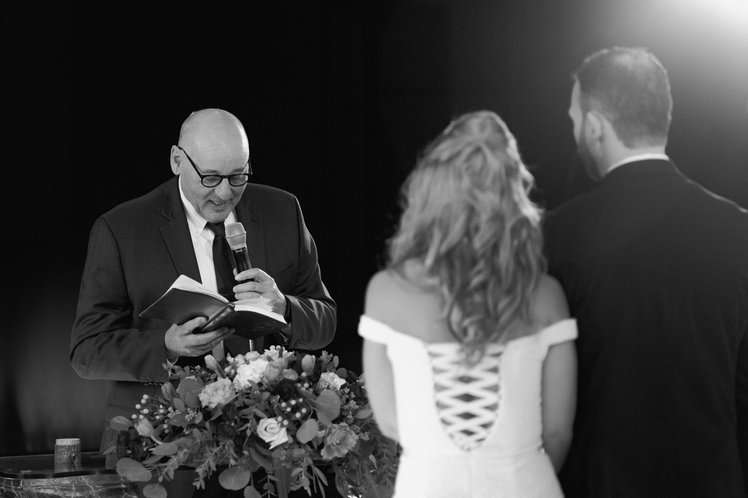 A wedding ceremony officiant reads from a book during an indoor service.