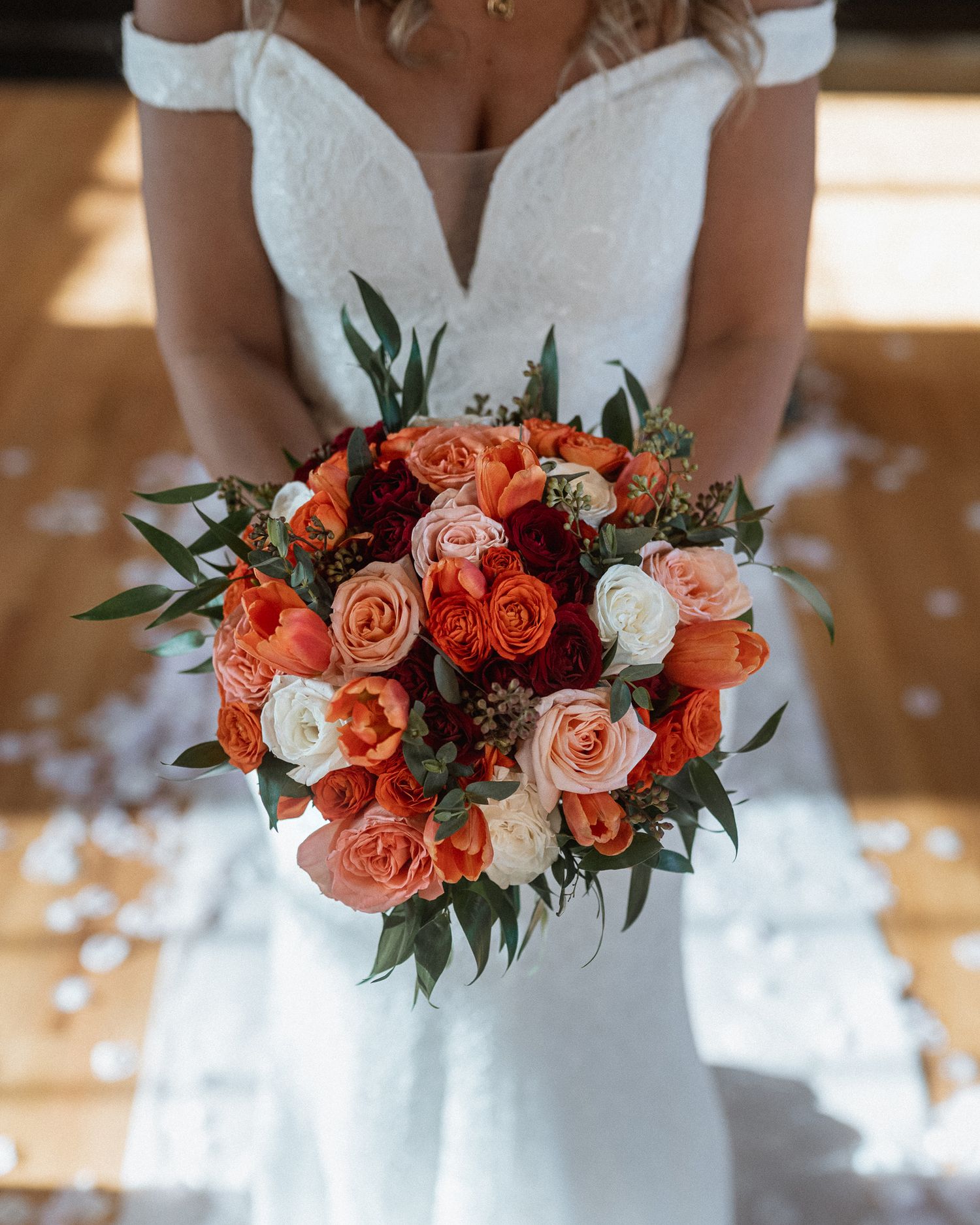 Beautiful bouquet of coral roses and white flowers with greenery against a white wedding dress.