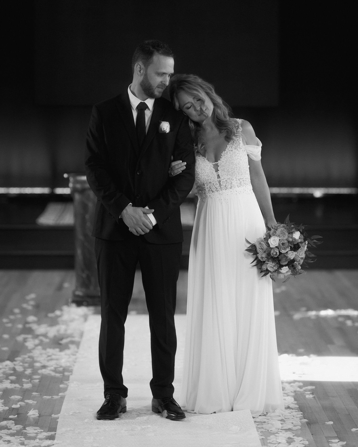 Black and white photo showing formal wedding attire and rose petals scattered on the floor.