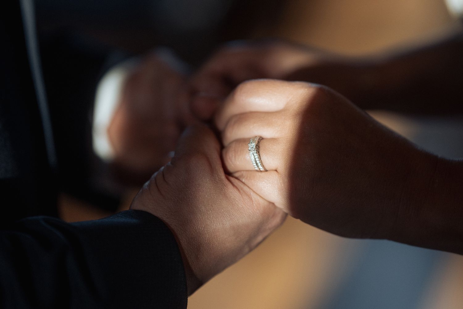 Close-up detail of hands and a sparkling engagement ring in soft lighting.