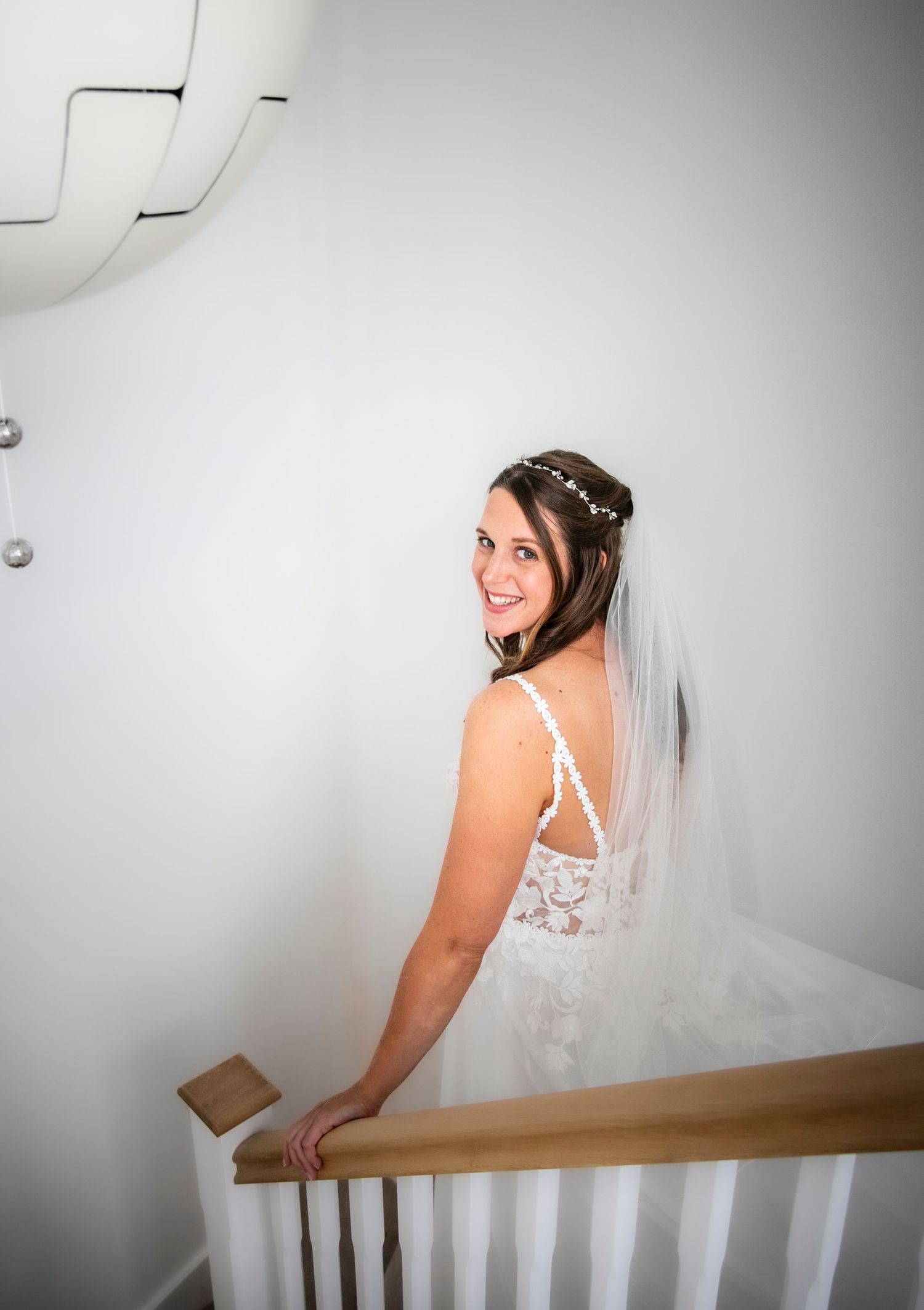 Bridal portrait on stairs showing wedding dress and veil details against white background.
