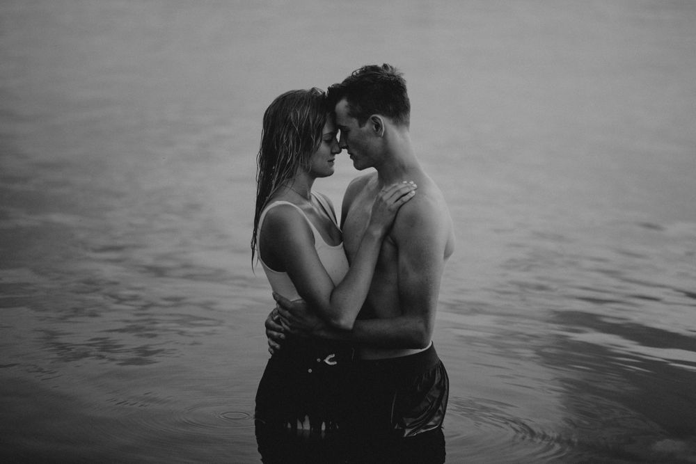 An intimate black and white portrait of two people embracing in water.