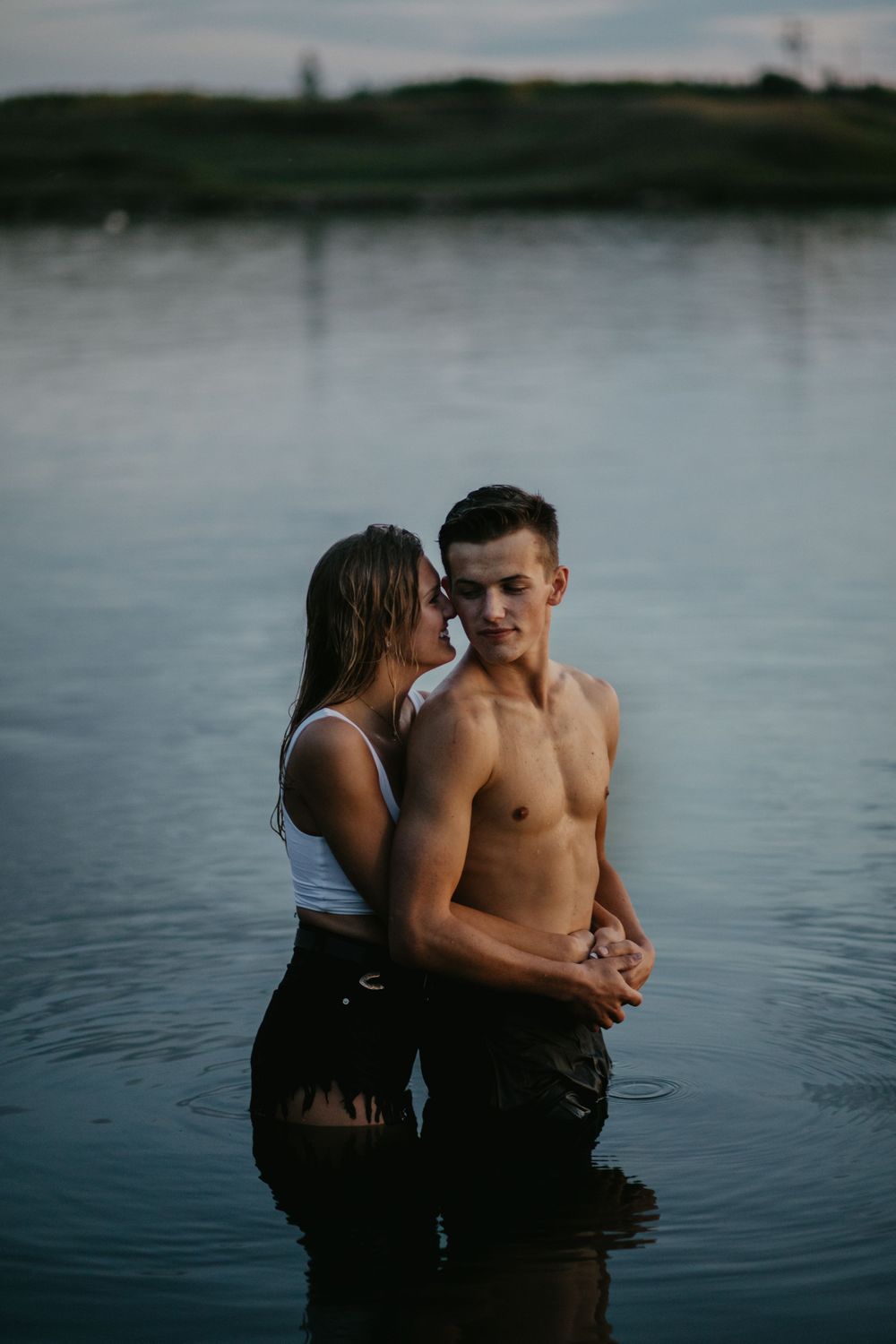 A couple stands together in lake water during a romantic sunset photoshoot.