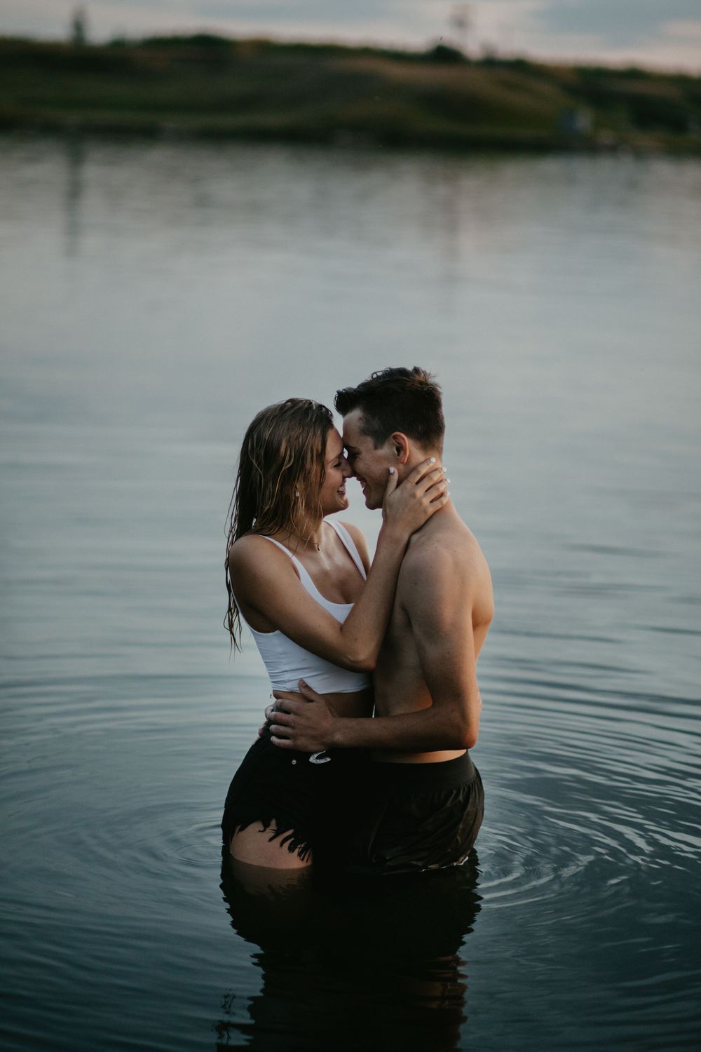 A couple shares an intimate moment while standing in a serene lake during sunset.