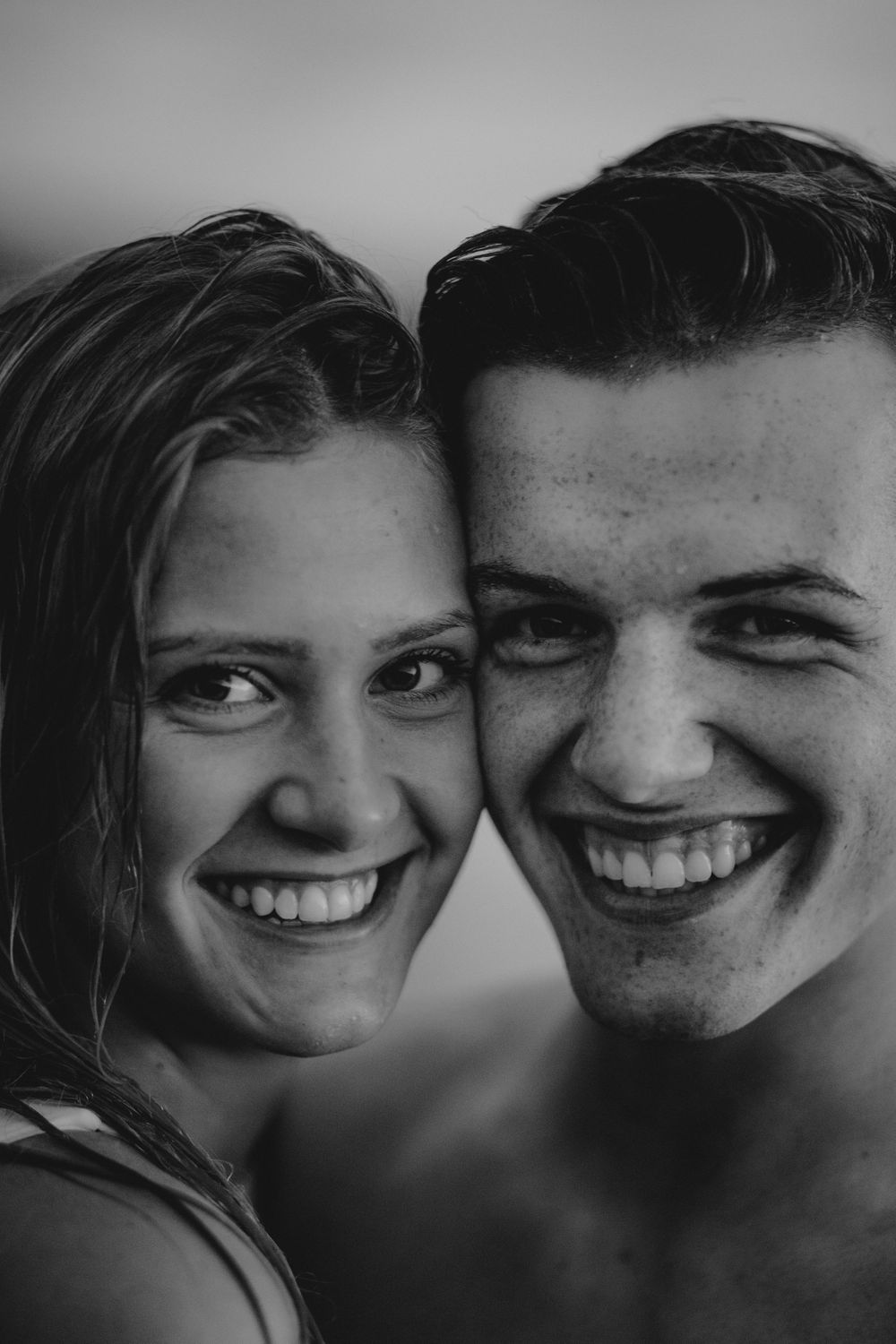 A black and white close-up portrait of two people smiling and enjoying a sweet moment together.