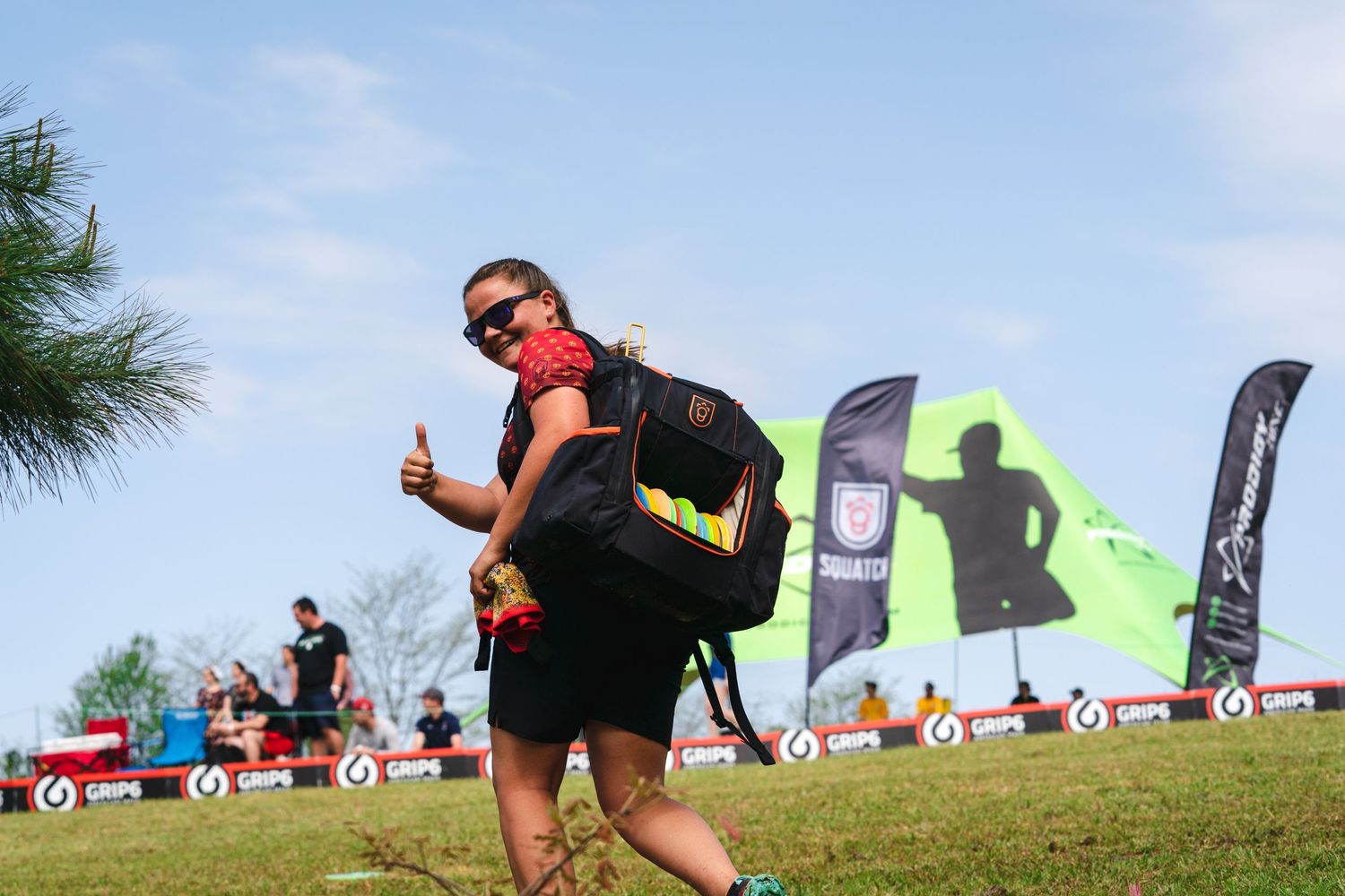 Pro disc golfer, Callie McMorran giving a thumbs up to the viewer while walking away. She's wearing her Squatch backpack