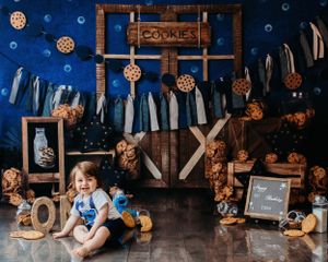 A rustic cookie-themed photo set with wooden decor, hanging denim, twinkling lights, and decorative cookie ornaments.