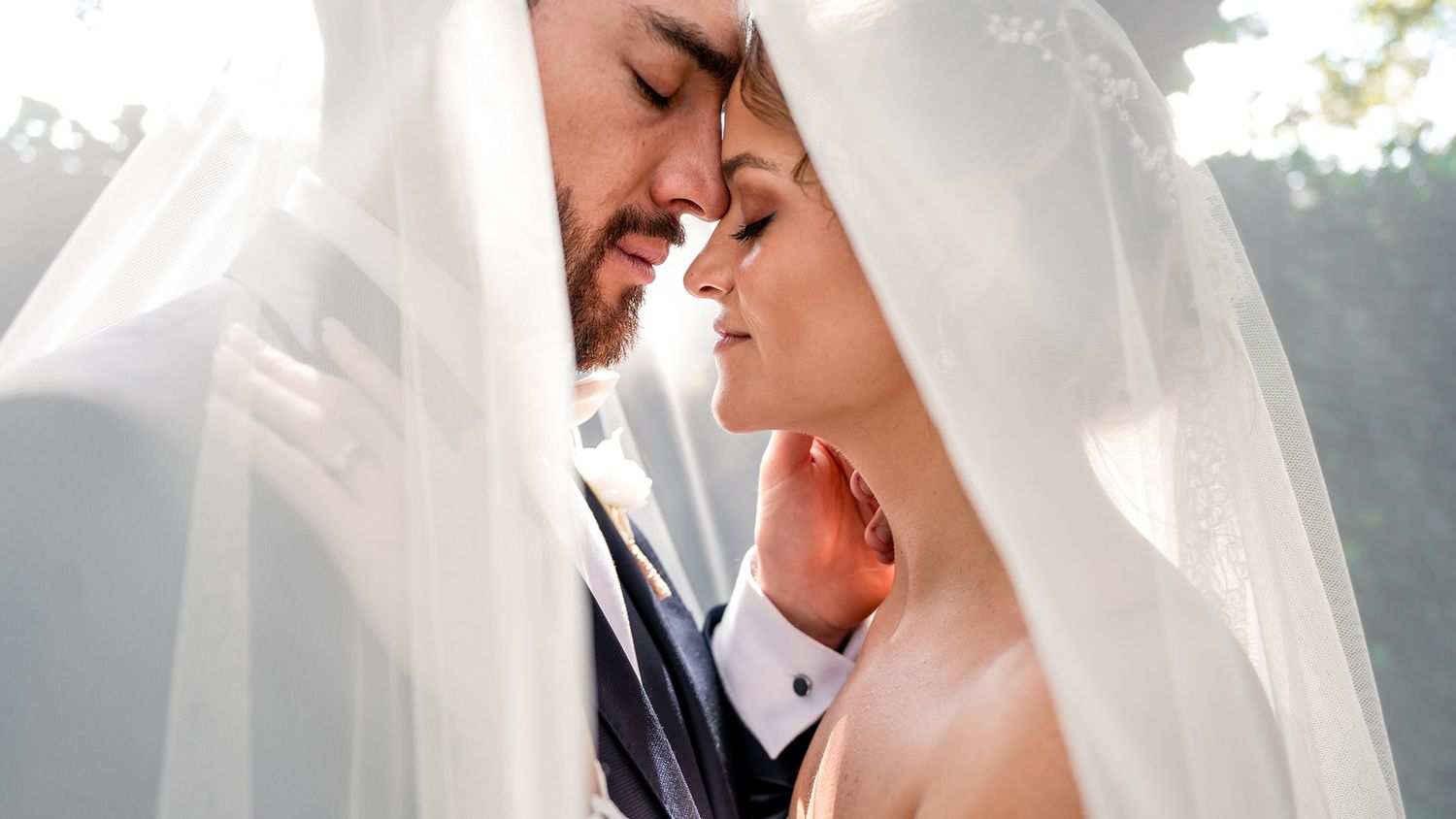 Romantic wedding portrait through delicate white veil in natural outdoor lighting.