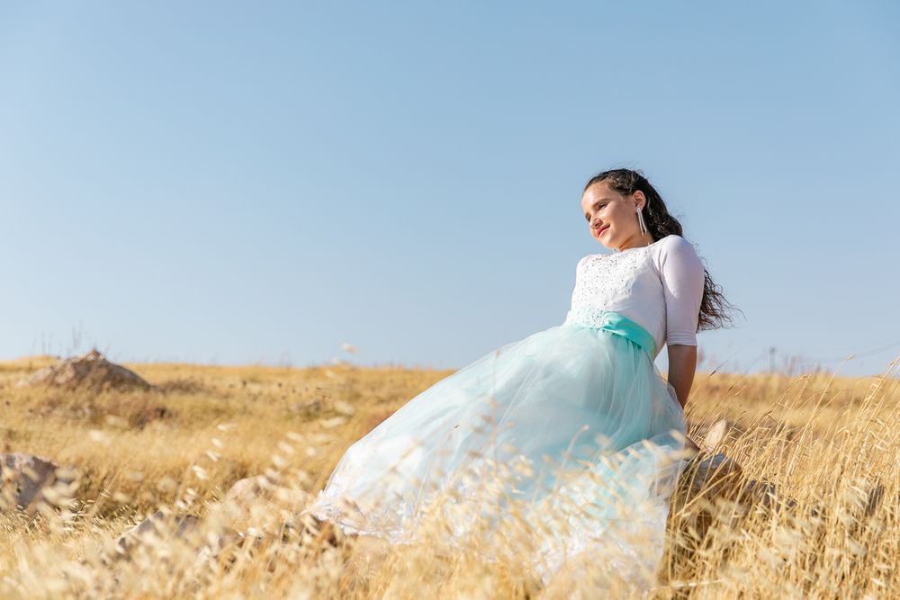 a beautiful girl sitting on a rock in the middle of a beautiful yellow field