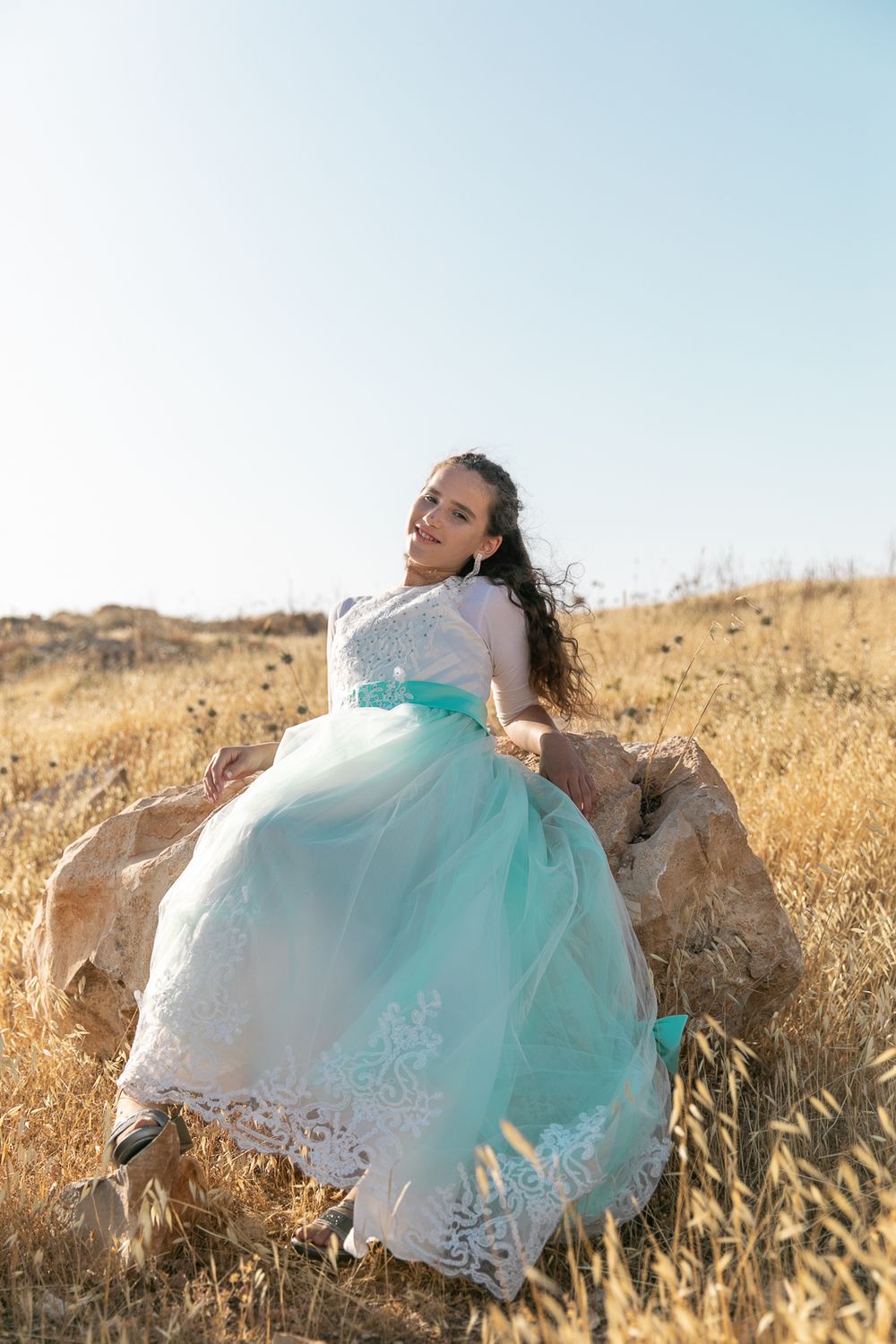 a beautiful girl sitting on a rock in the middle of a yellow field