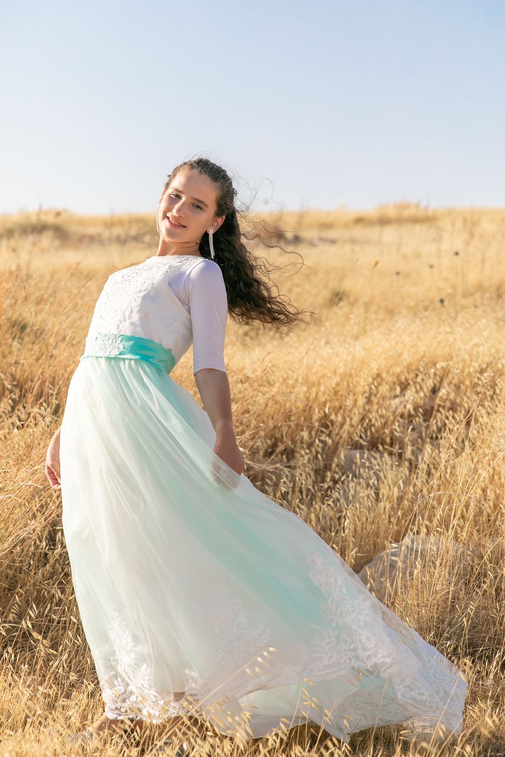 A girl with a beautiful light blue dress standing in the middle of a yellow field
