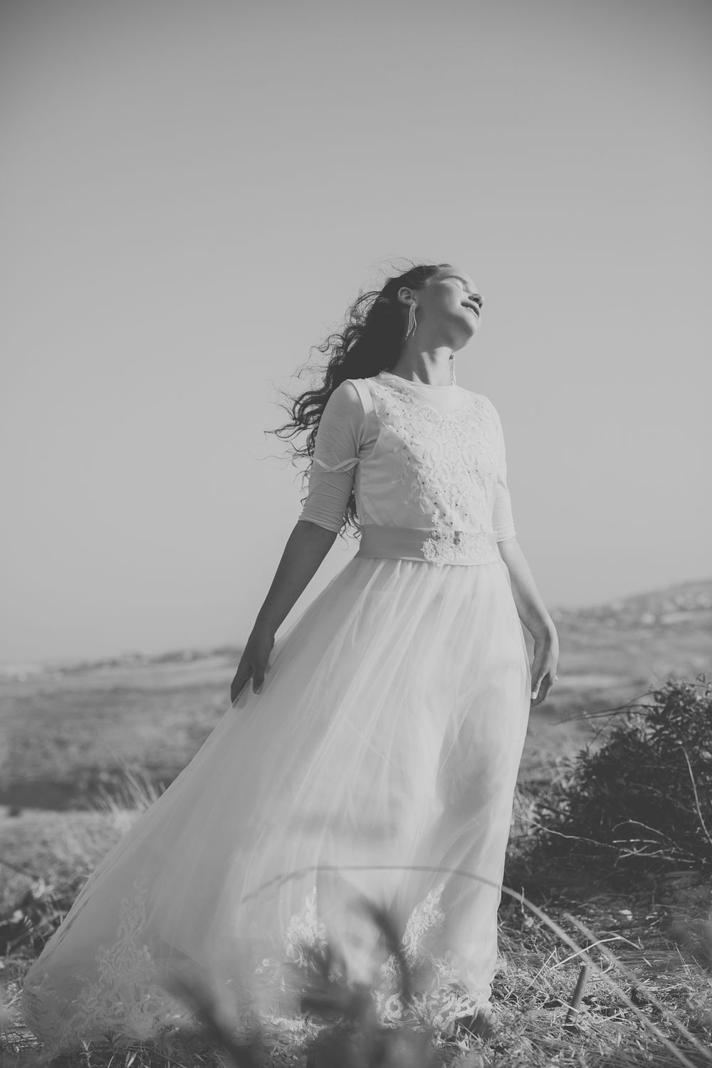 a black and white picture of a girl with a beautiful dress standing in the middle of a yellow field