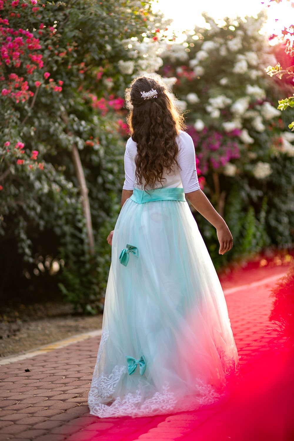 A beautiful girl stands with her back to the camera and in the background colorful flowers