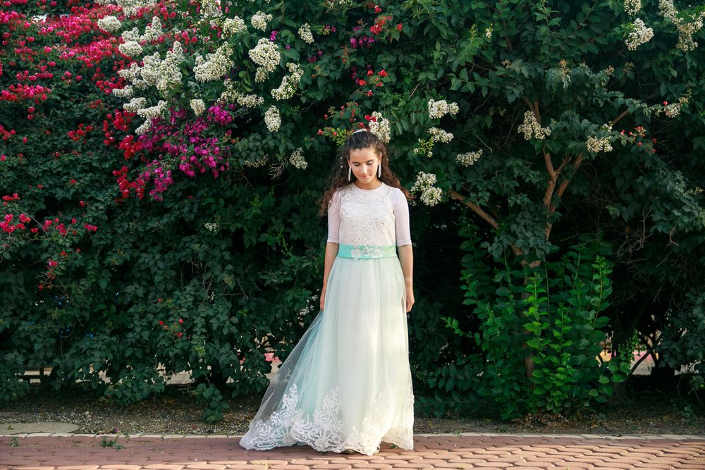 A beautiful girl stands on the path and in the background colorful flowers