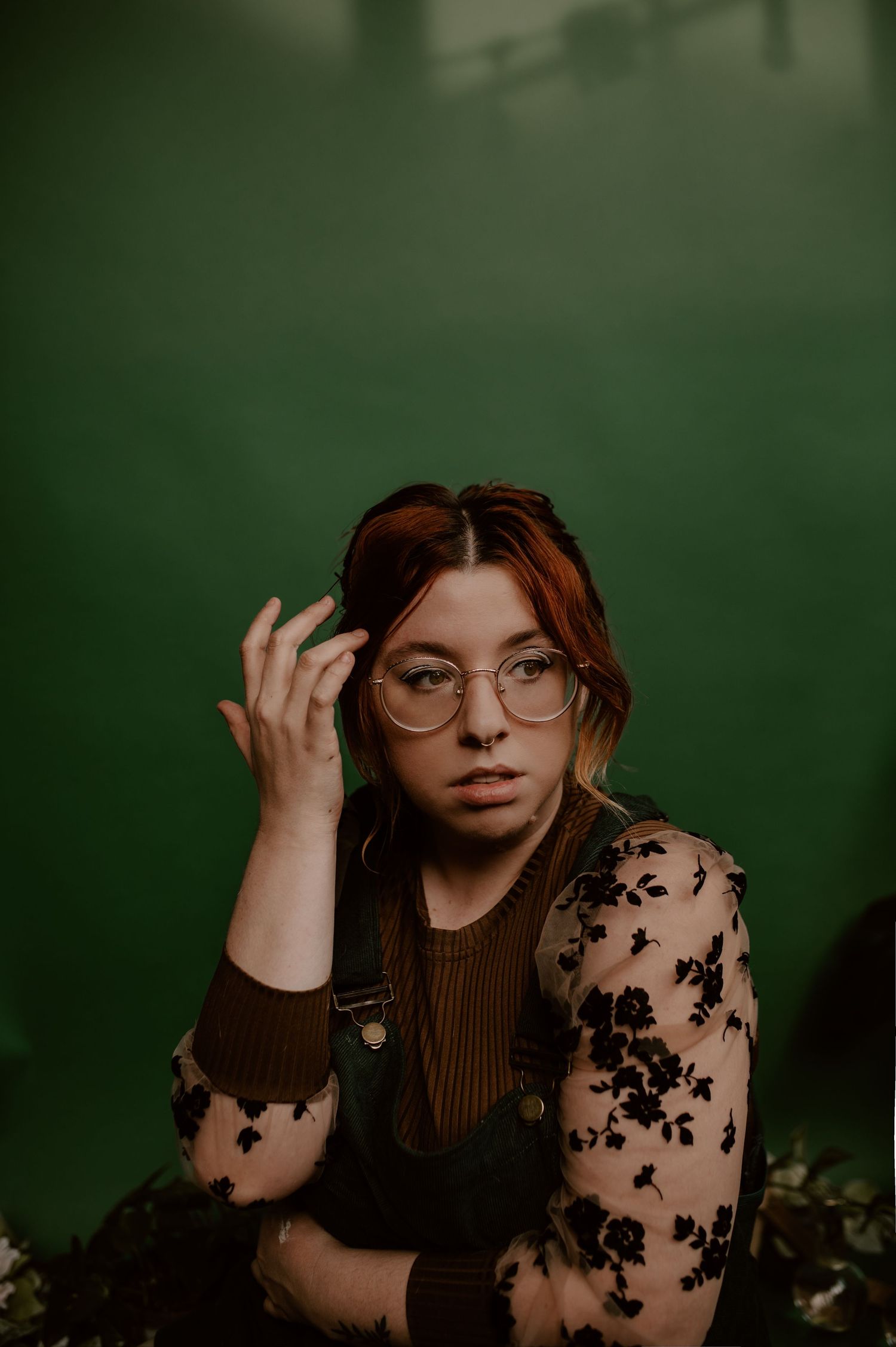 A contemplative portrait featuring round glasses and delicate floral sheer sleeves against green.