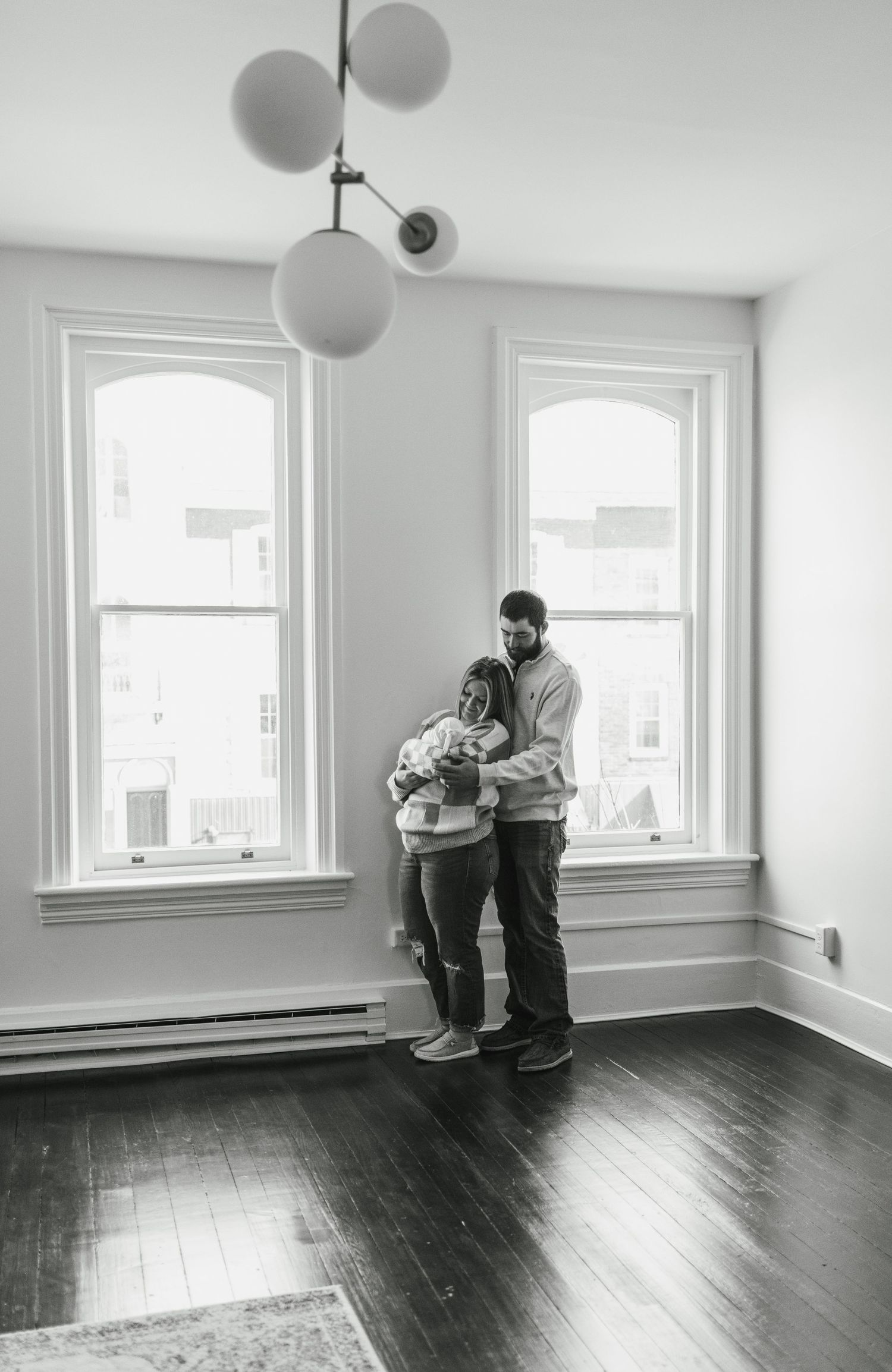 Black and white portrait in empty room with globe pendant lights and tall windows.