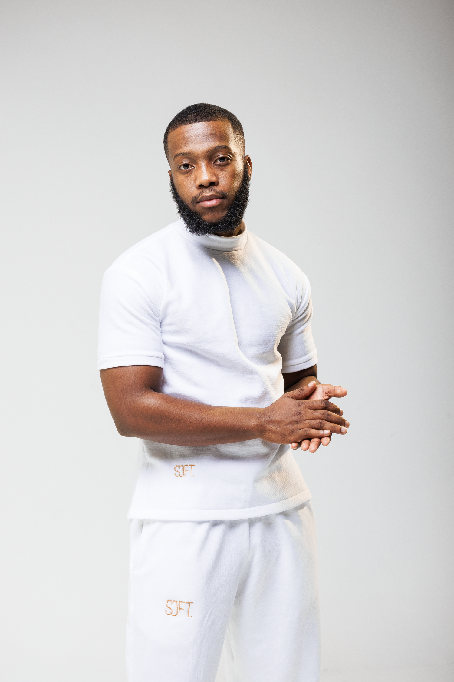 Athletic figure in all-white outfit poses against light gray studio background.