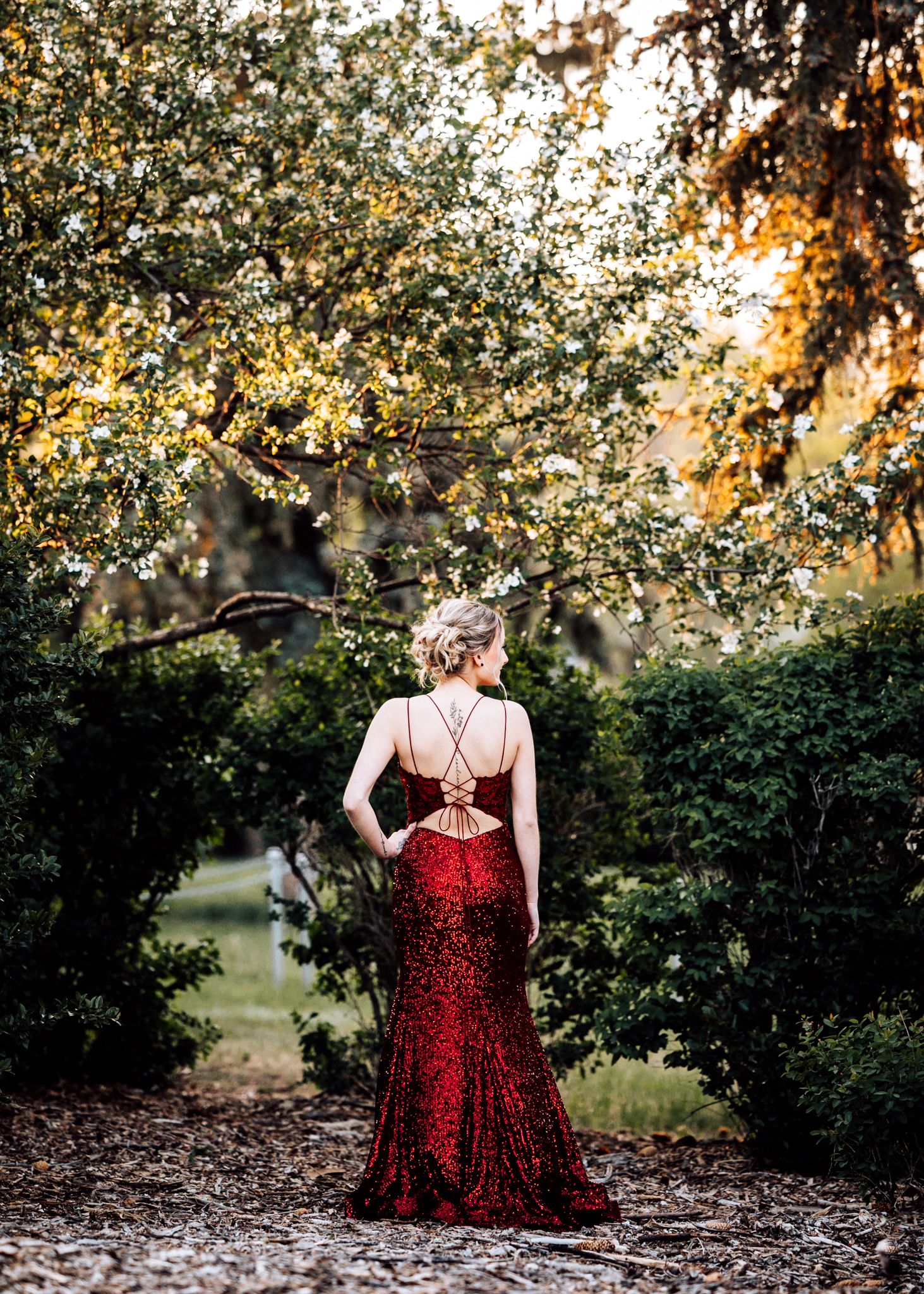 Elegant woman in a stunning red sequin gown posing in a lush garden at golden hour.