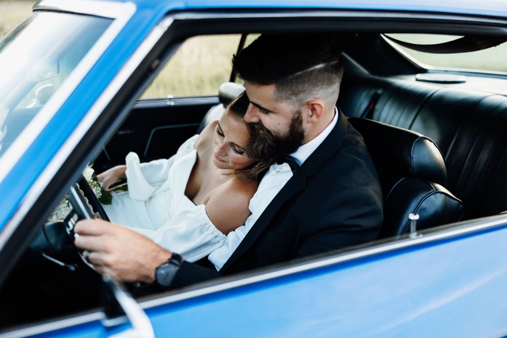 A romantic moment shared between newlyweds in a classic blue car with vintage interior.