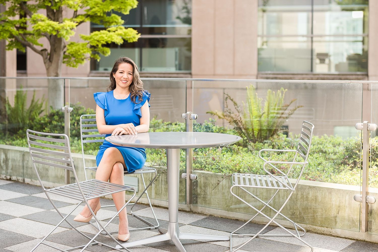 A woman wearing a blue dress sits outside the library at a patio table.