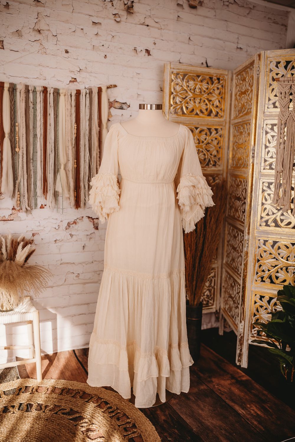 Cream lace ruffle sleeve boho maxi dress on mannequin in rustic white brick studio setting.