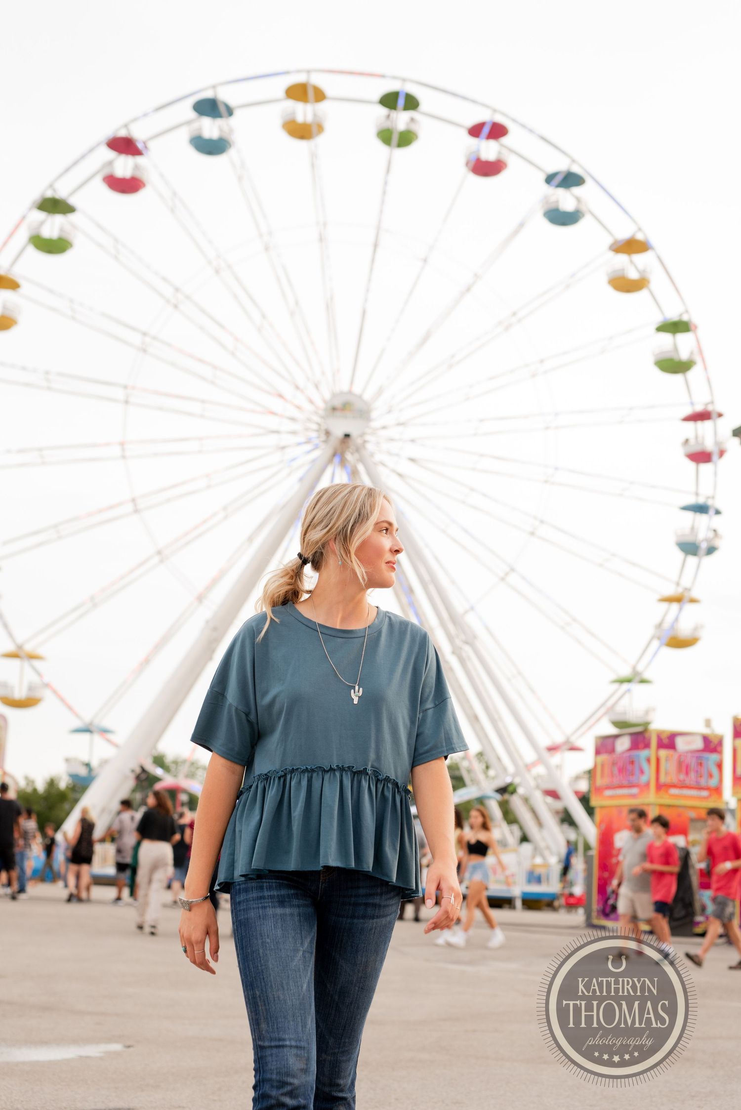 Candid shot of someone in a blue peplum top posing with a giant ferris wheel in the background.