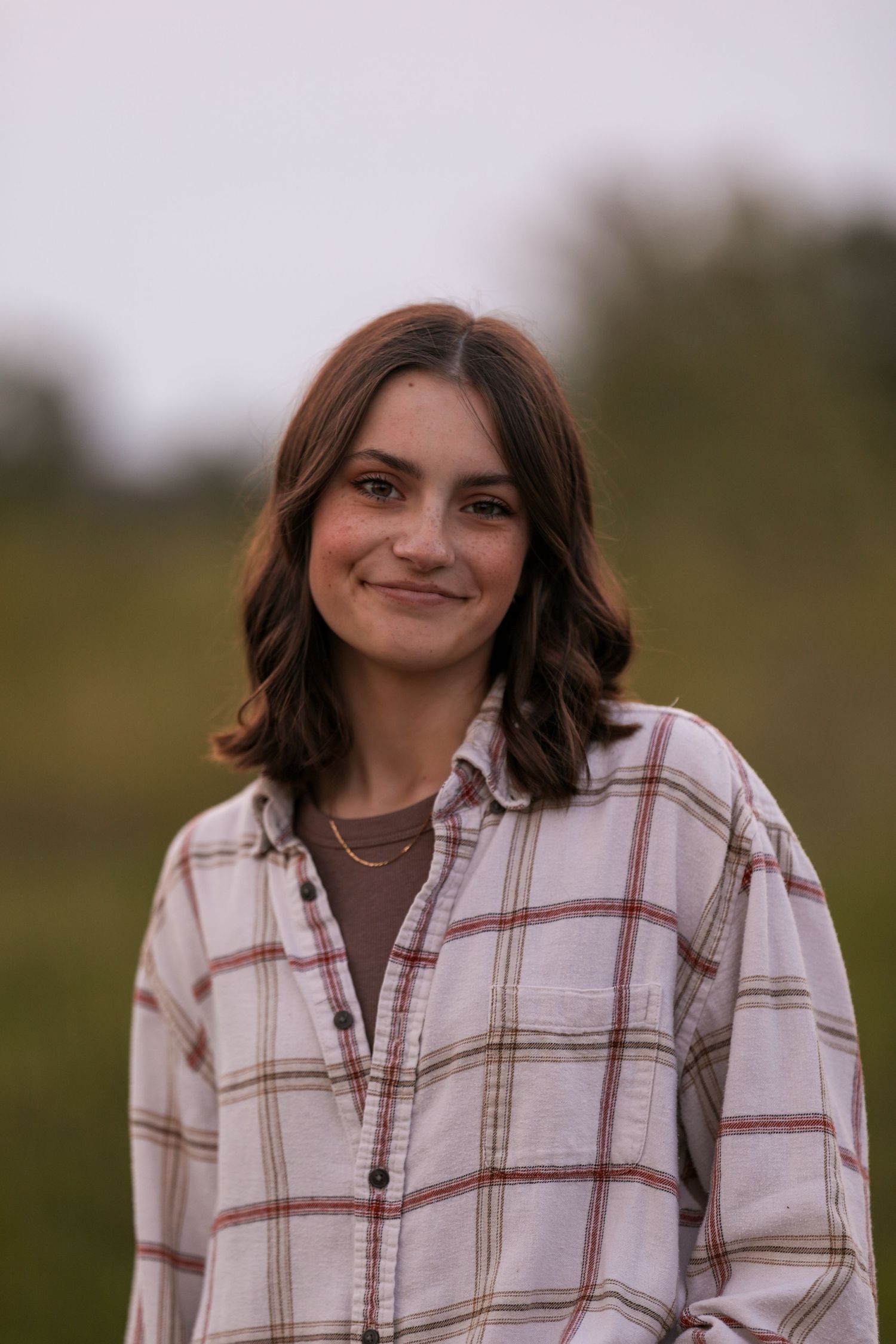 Person in plaid flannel shirt smiles against blurred natural background.