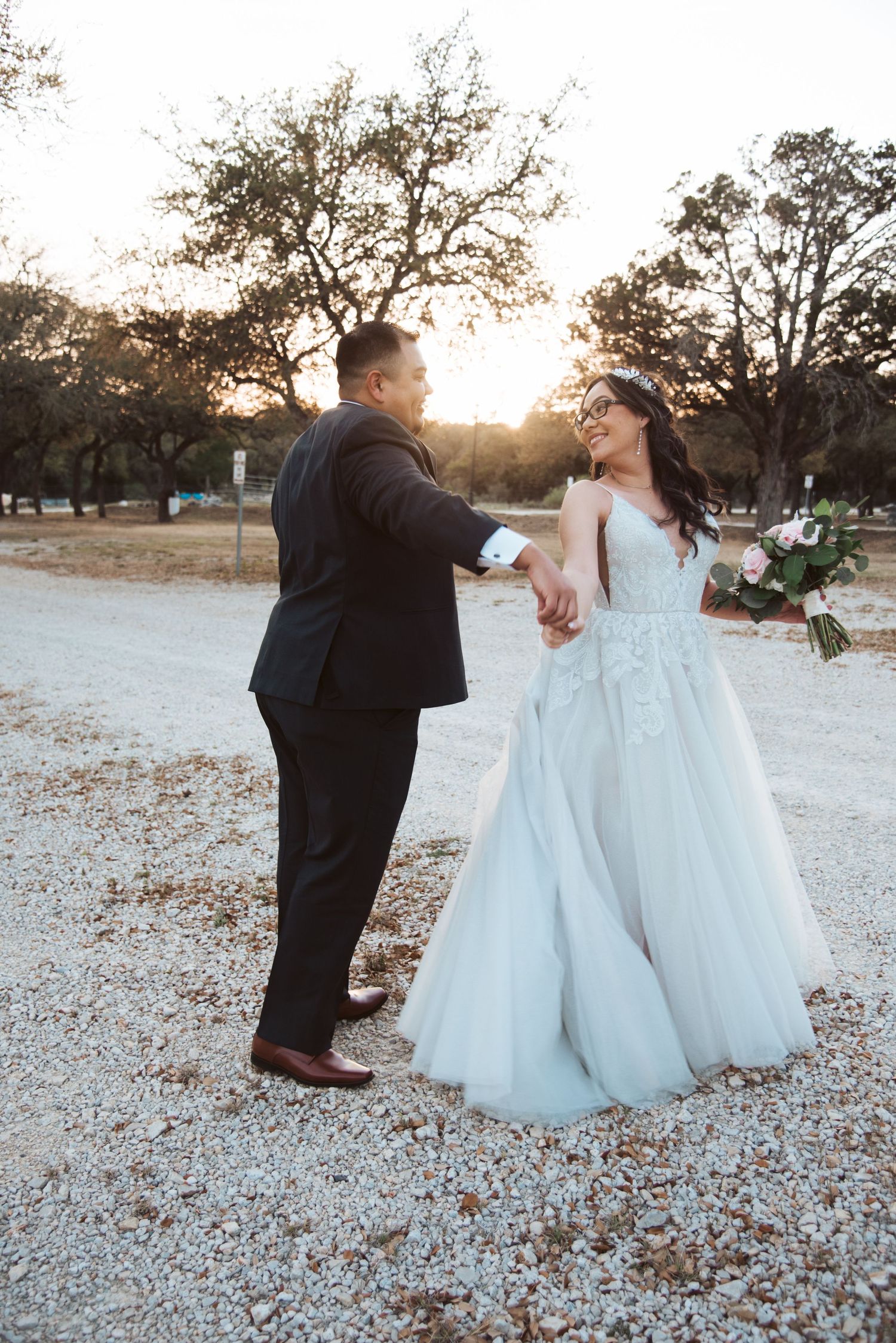 Couple dancing together on a gravel path during golden hour with trees silhouetted in background.