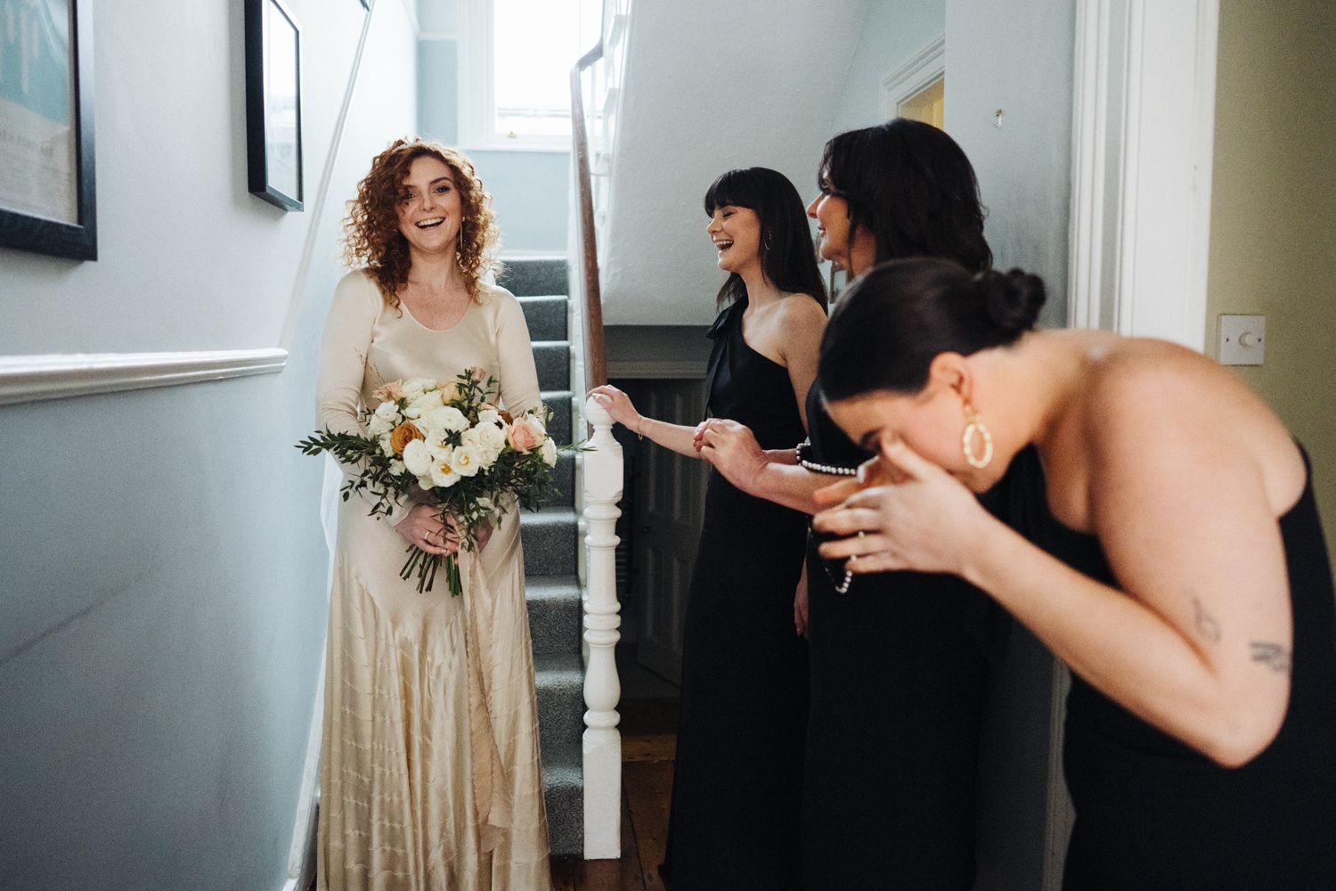Wedding party in black dresses reacting with excitement in stairwell.