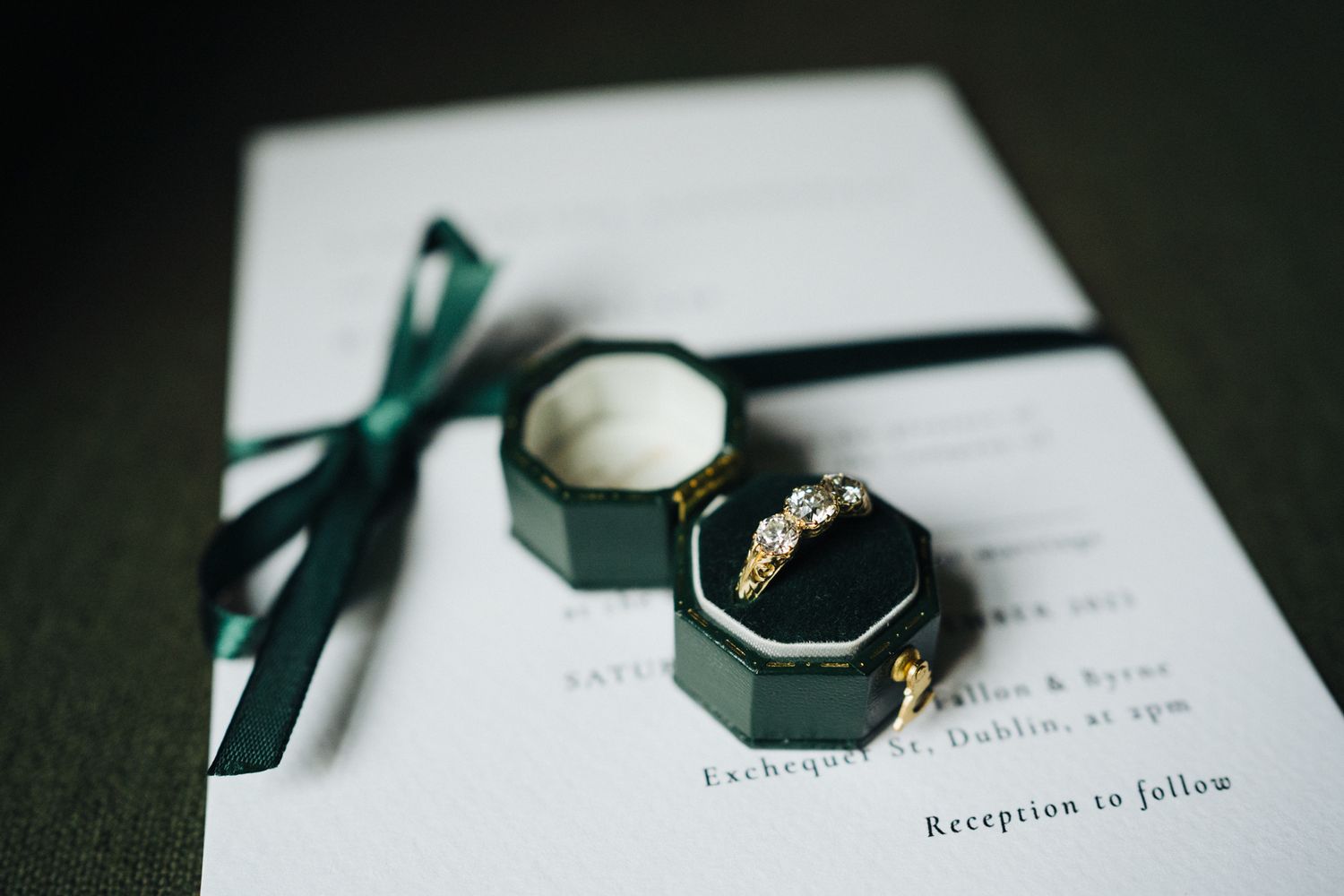 Wedding rings and invitation displayed with emerald green ribbon in an elegant box.