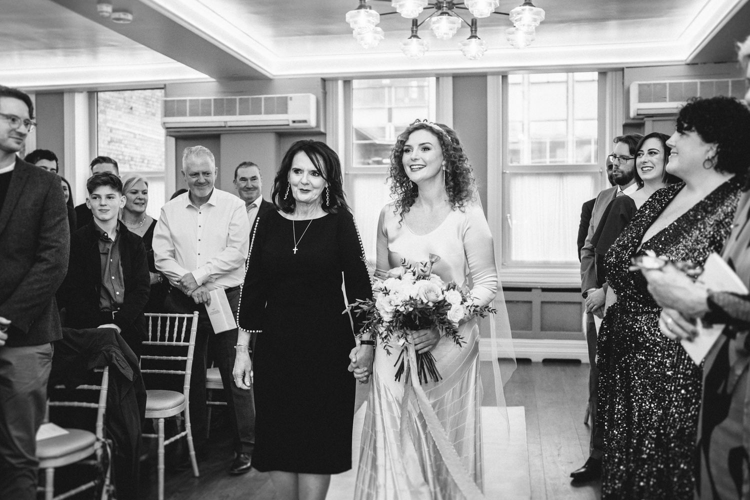 A black and white photo of guests watching a wedding ceremony in an elegant indoor venue.