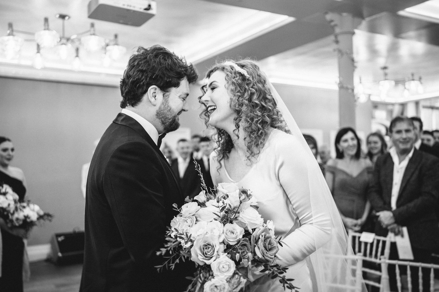 A joyful black and white photo of a couple sharing a laugh during their wedding ceremony.
