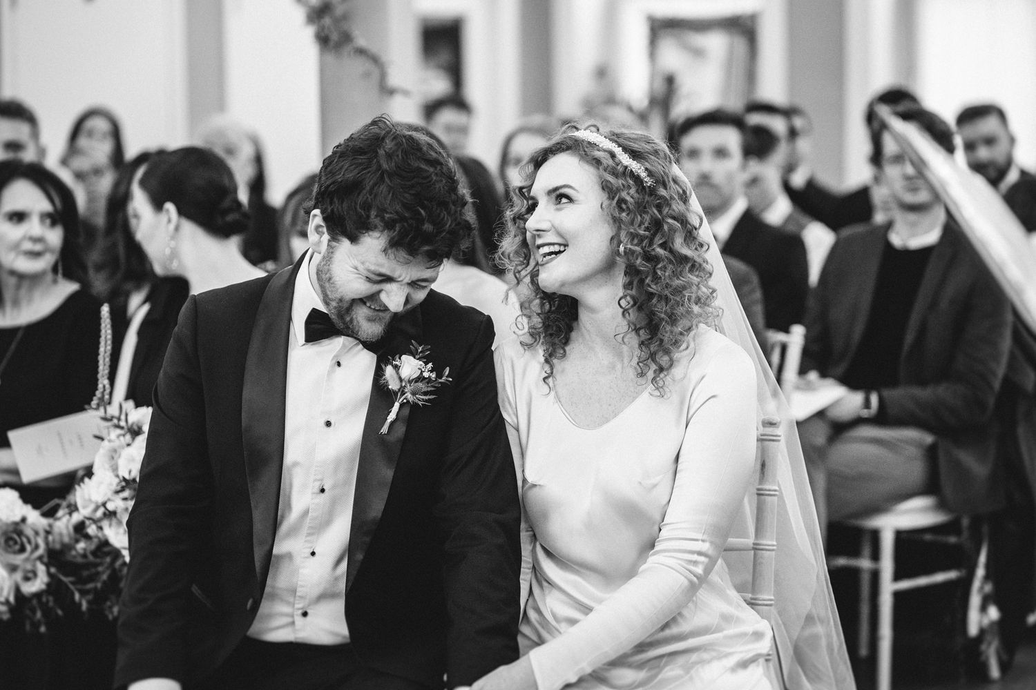 A candid black and white photo of a couple sharing a happy moment during their wedding ceremony.