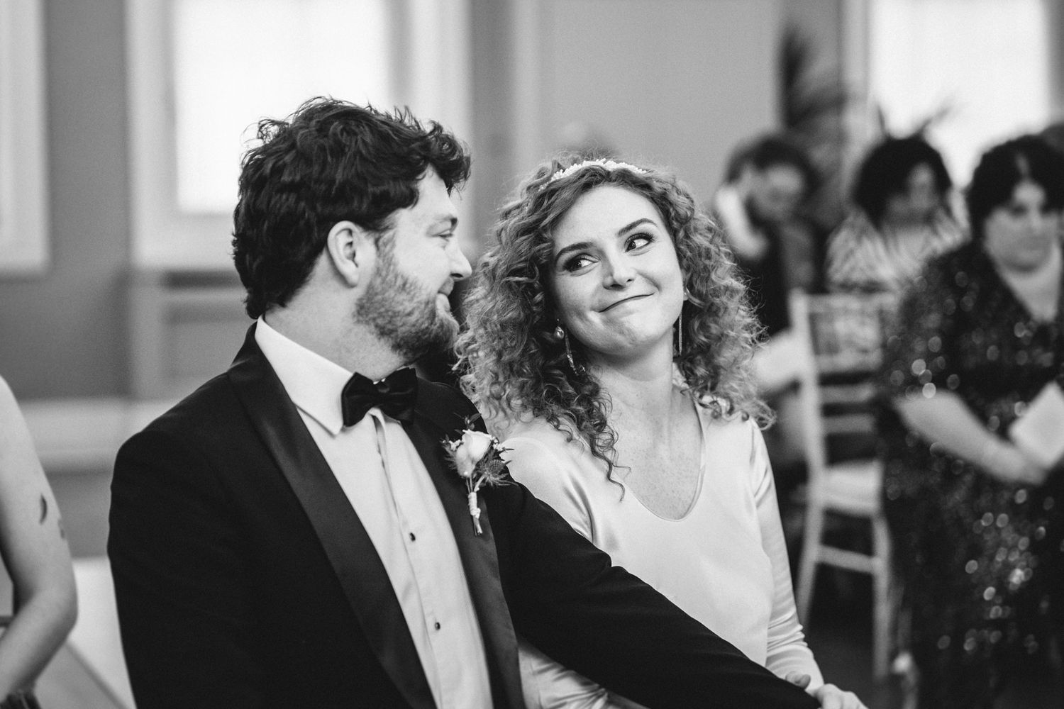 A candid black and white moment of a couple sharing laughter during their wedding ceremony.
