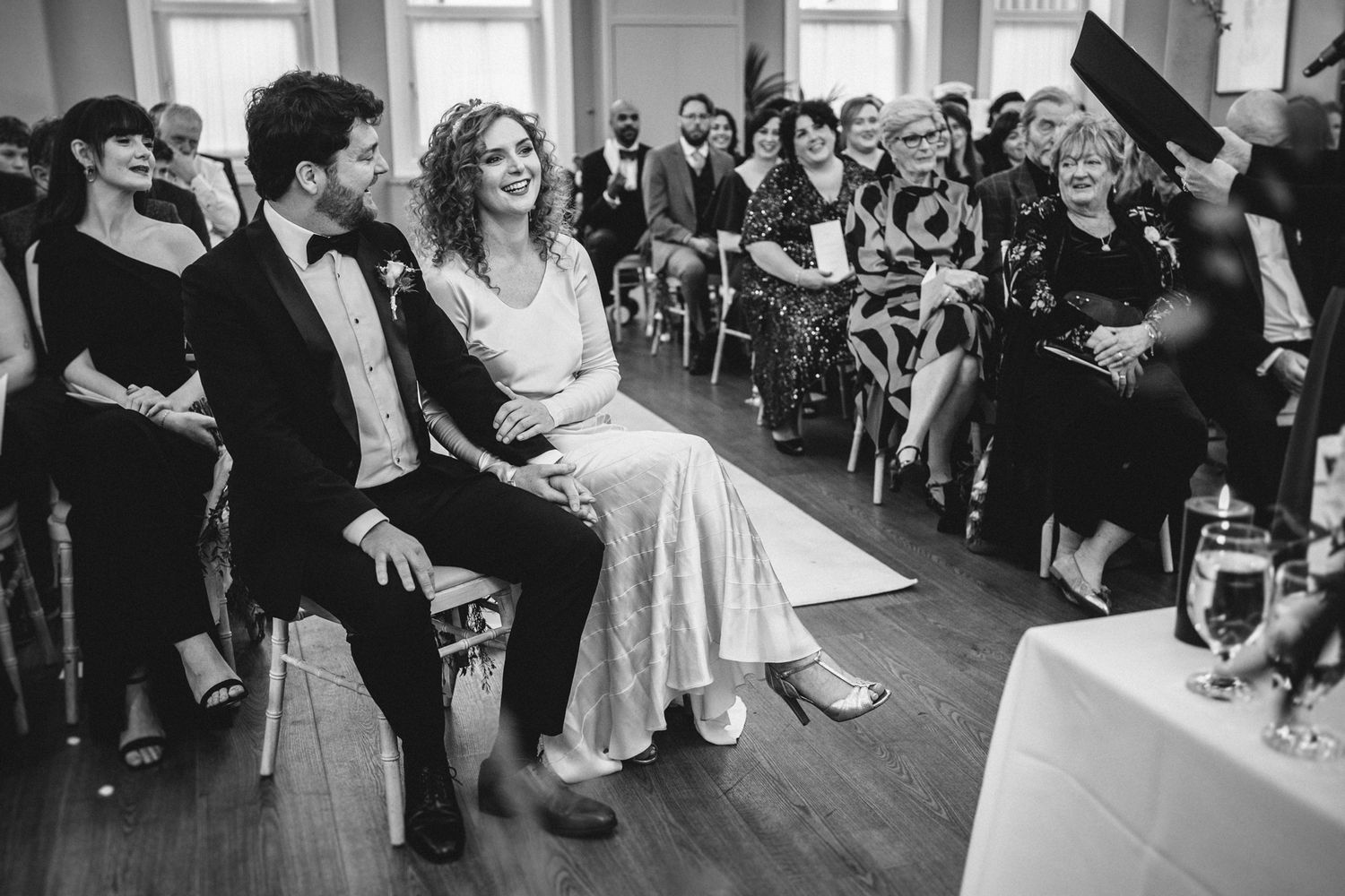 Black and white photo of a wedding ceremony with guests seated in rows watching the proceedings.
