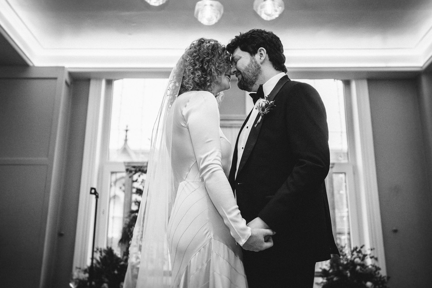 Romantic black and white moment between newlyweds holding hands during their ceremony.