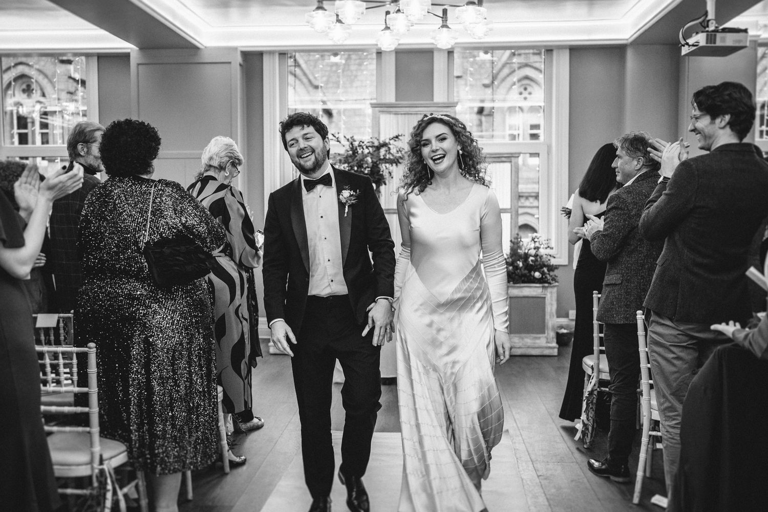 Couple walks down the aisle as married while guests look on in a beautifully lit venue.