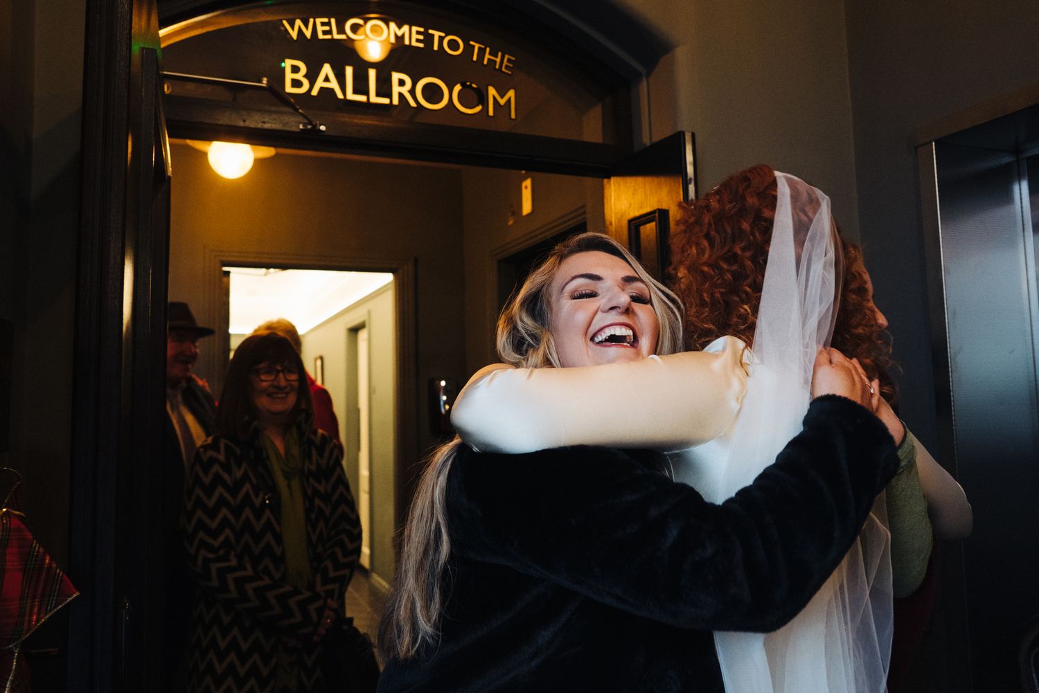 Wedding celebration with joyful hugging at the ballroom entrance.