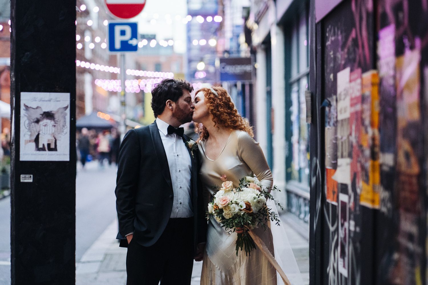 Newlyweds share an intimate moment in an urban alley with colorful street art visible.