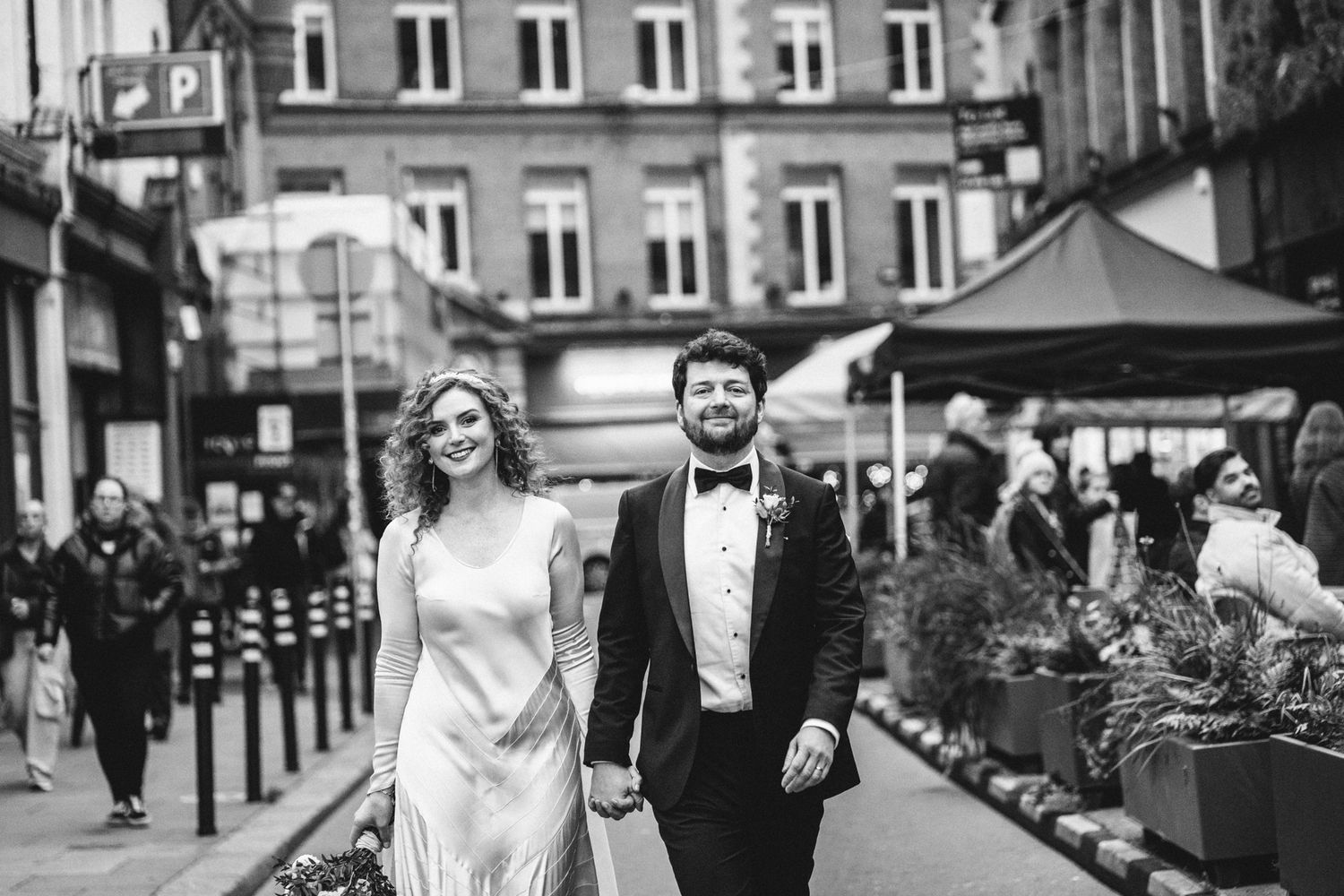 A black and white wedding photo of a couple walking through a busy city street with pedestrians.