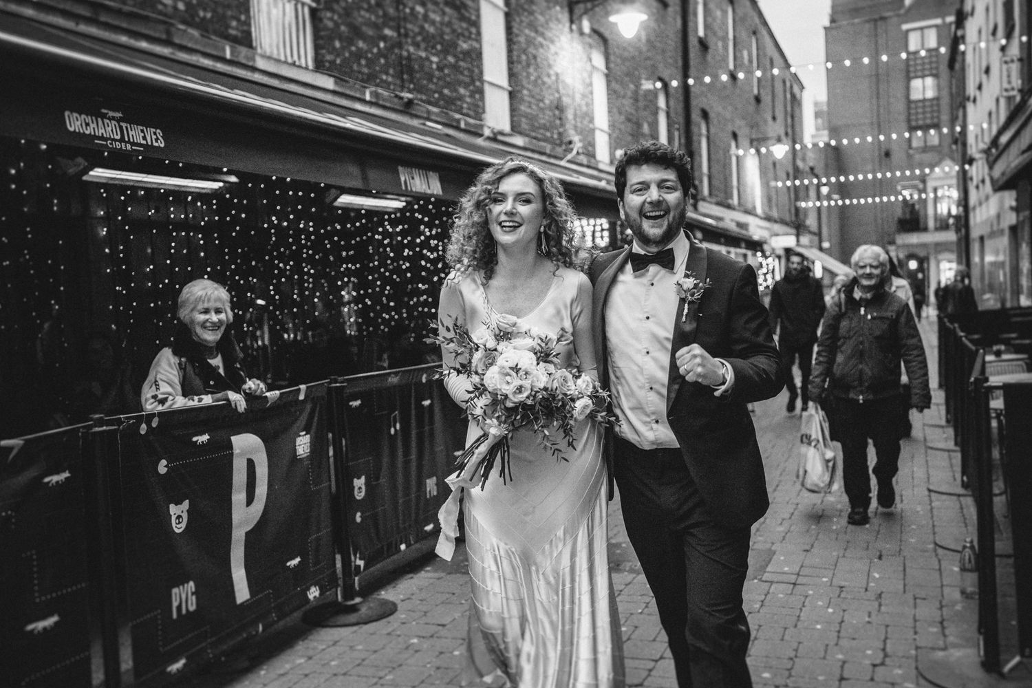 A couple joyfully walking down a string-lit street during an urban celebration.