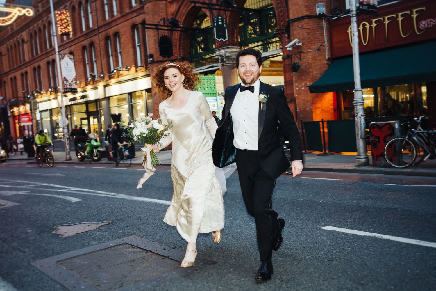 A couple running playfully down a city street lined with shops and restaurants.