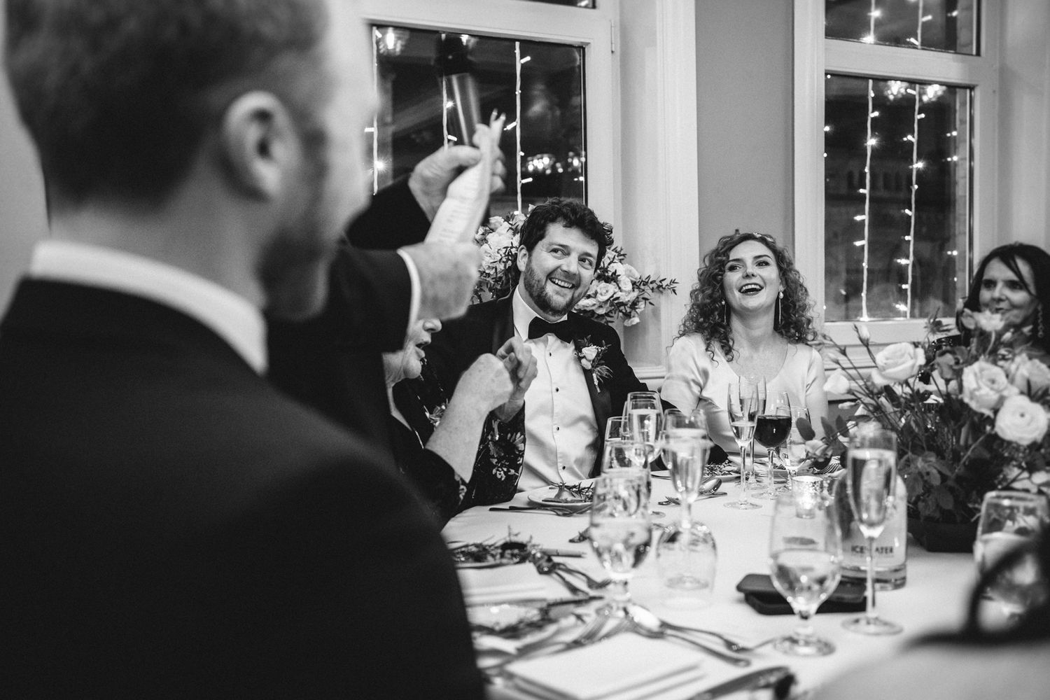 Wedding guests raise glasses in celebration during an indoor reception dinner.