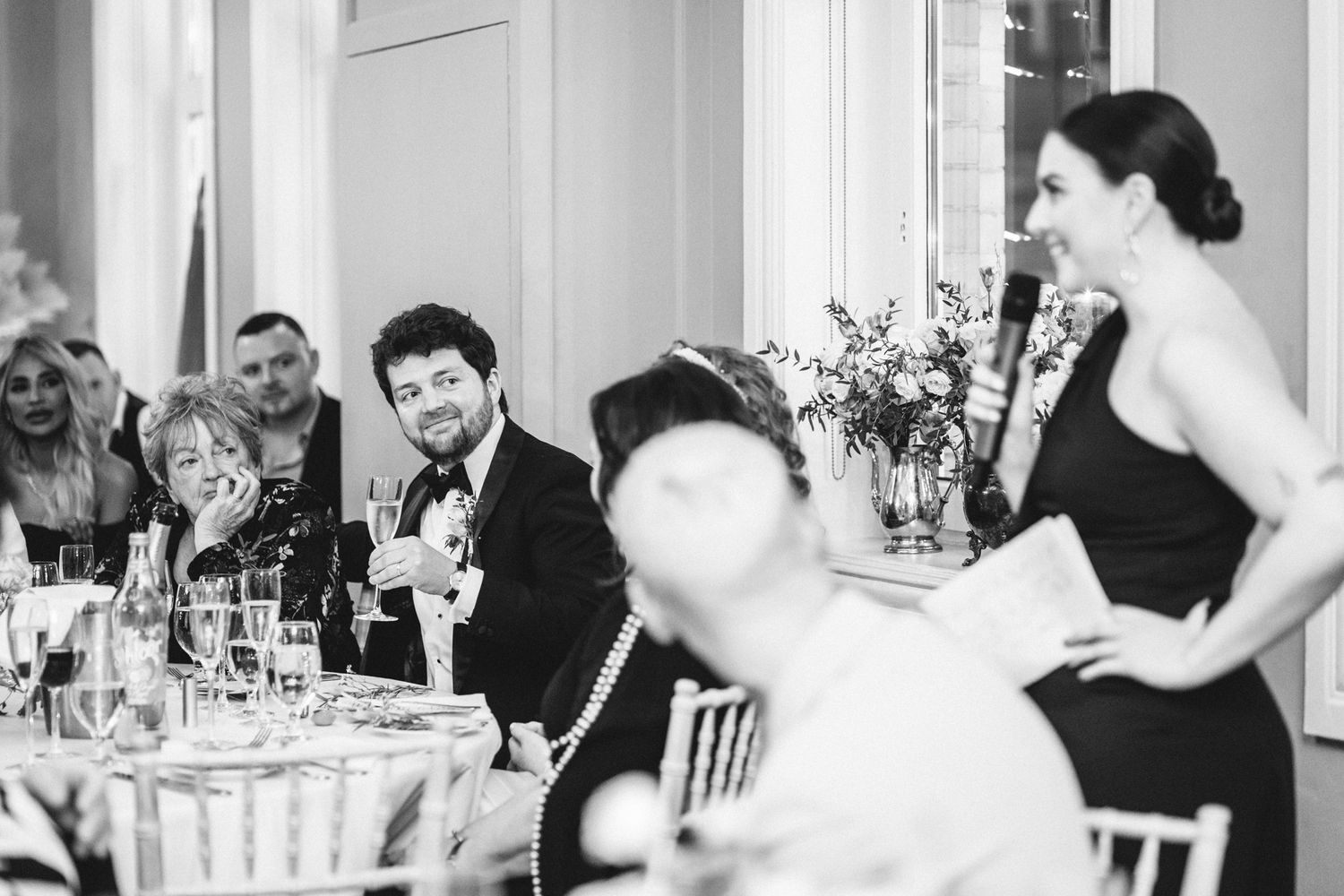 Black and white photo of guests enjoying a lively moment during an elegant wedding dinner reception.