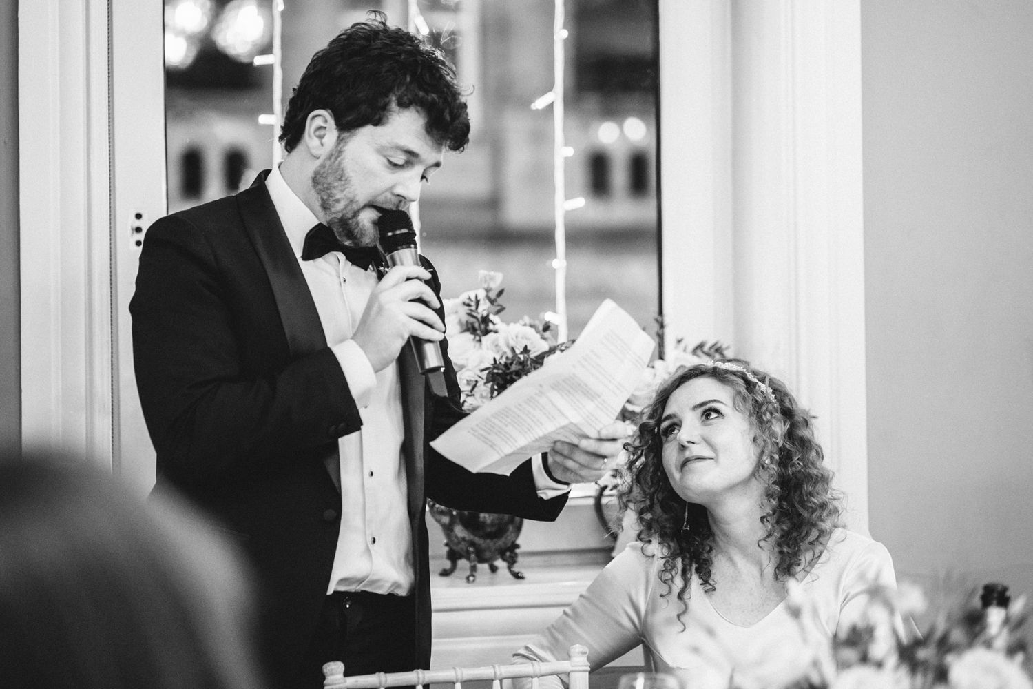 Black and white candid photo showing a speech being delivered at a wedding reception.